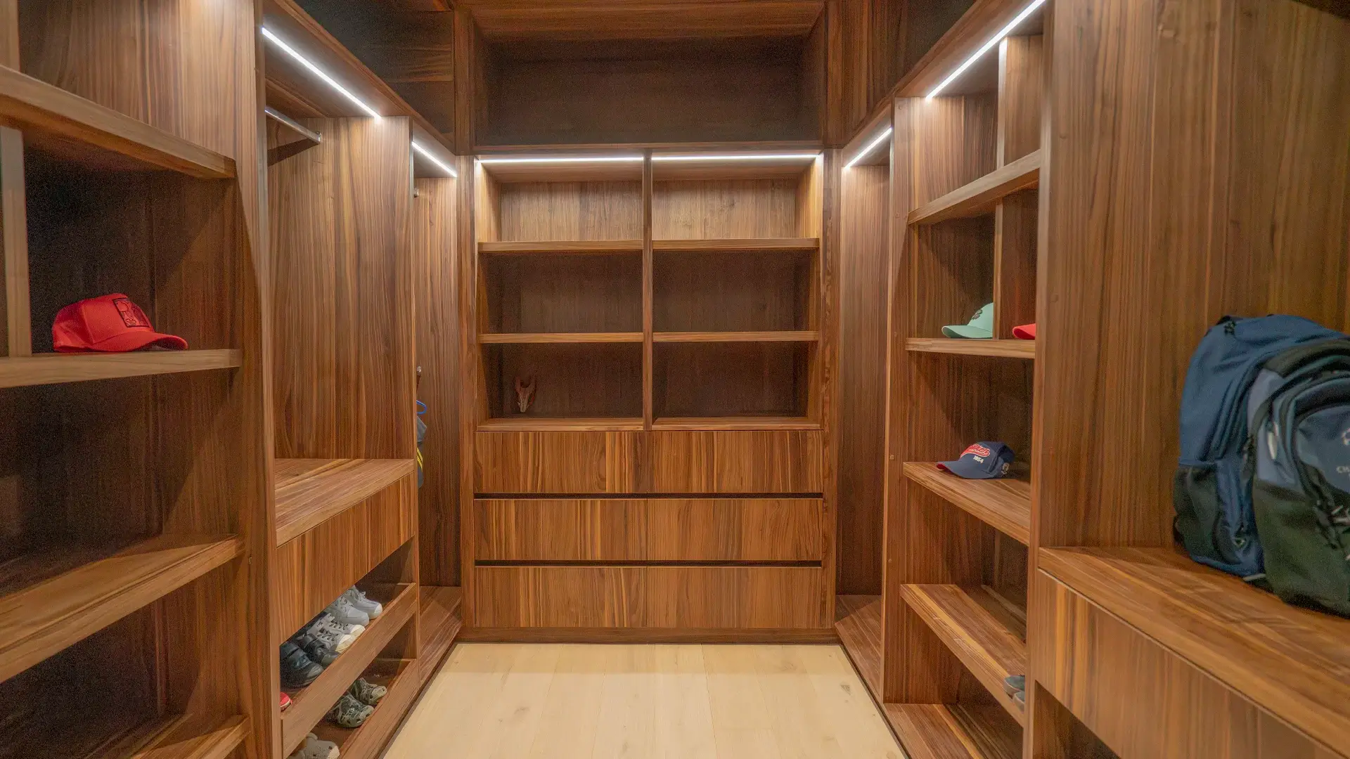Clóset vestidor (walk-in) a medida de Casa Iktan en Querétaro, en madera tono nogal, con iluminación LED integrada, repisas laterales, cajoneras centrales y módulos abiertos para organización diaria.